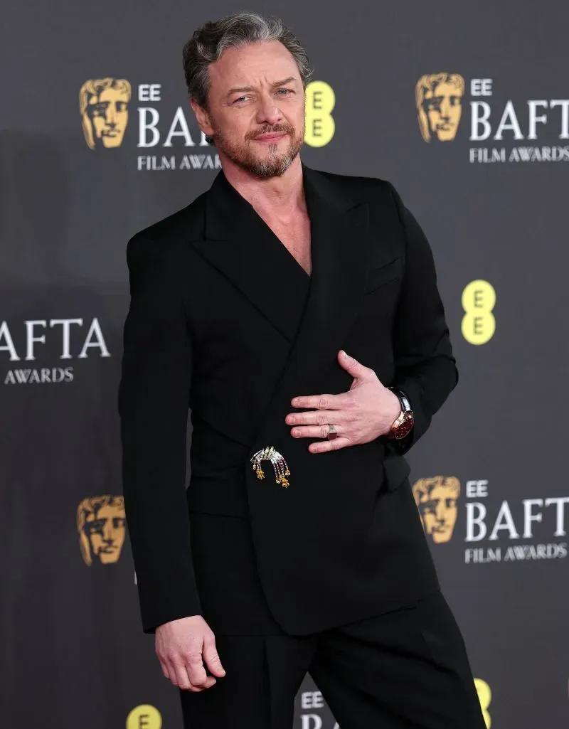 جيمس ماكافوي يرتدي بدلة سوداء أنيقة ويبتسم خلال حفل جوائز BAFTA، مع خلفية تحمل شعار الحدث.