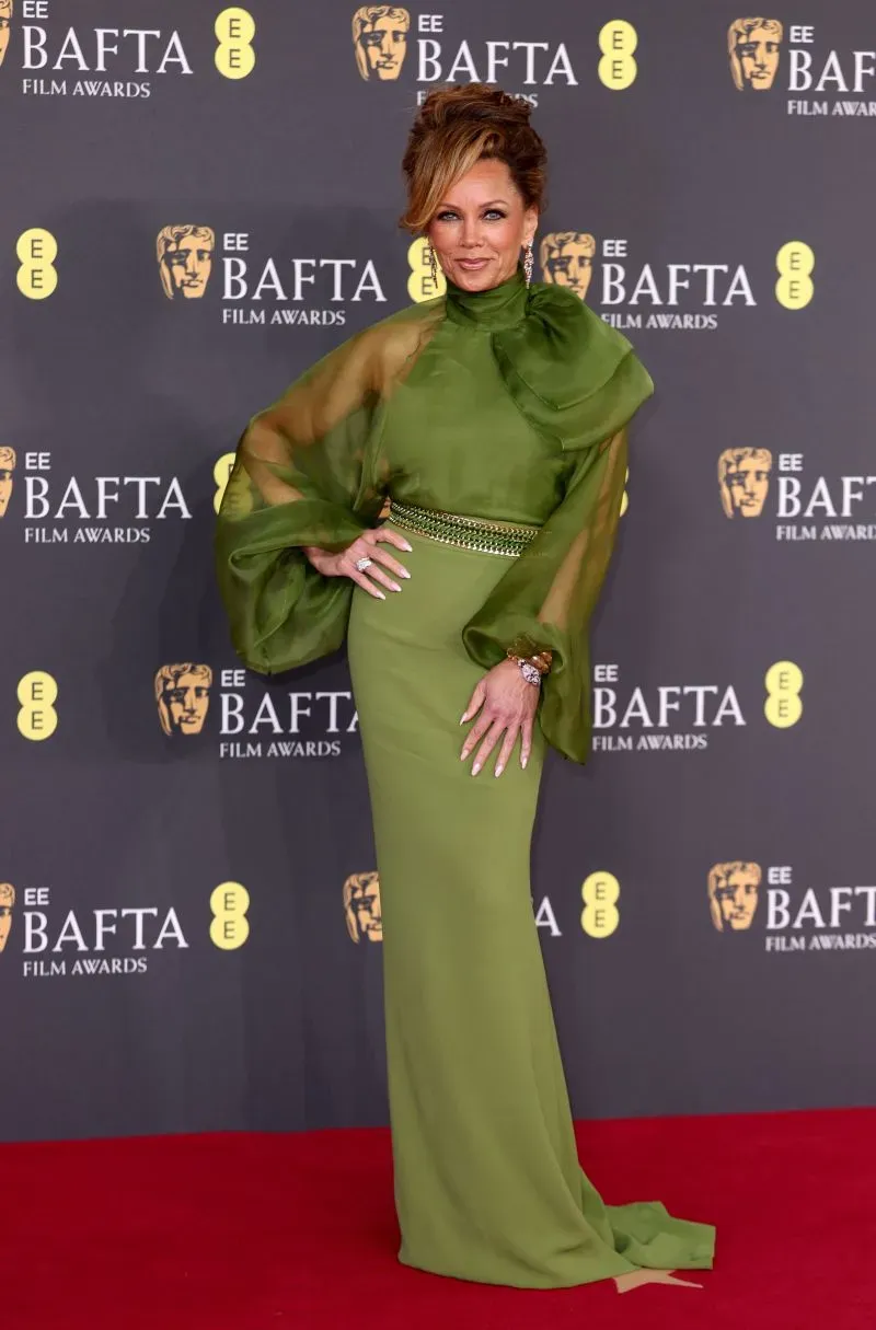 ممثلة ترتدي فستاناً أخضر أنيقاً مع أكمام شفافة، تتوسط حفل جوائز BAFTA في لندن، مع خلفية تحمل شعارات الحدث.