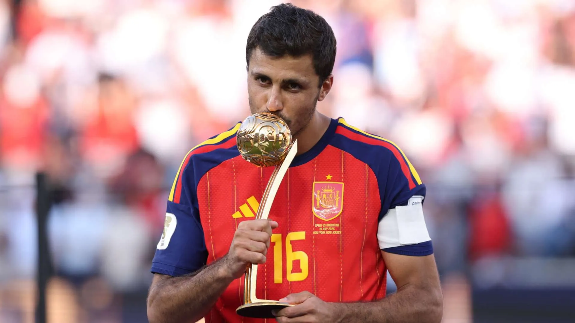 لاعب كرة قدم إسباني يرتدي قميص منتخب بلاده الأحمر يقبل جائزة الكرة الذهبية بعد الفوز بكأس العالم 2026.