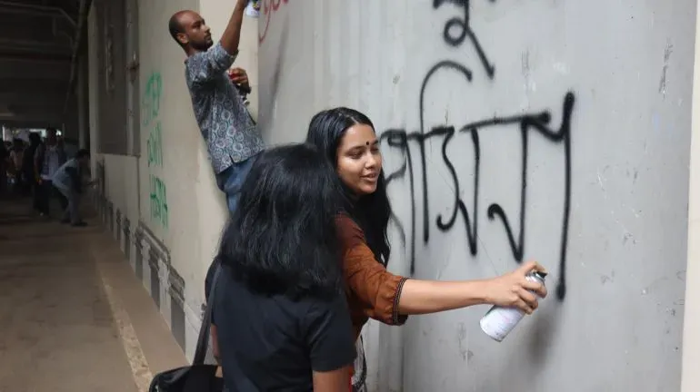 شباب يكتبون شعارات احتجاجية على جدار باستخدام علب الرش، مع التركيز على التعبير عن الغضب ضد الحكومة في بنغلاديش.