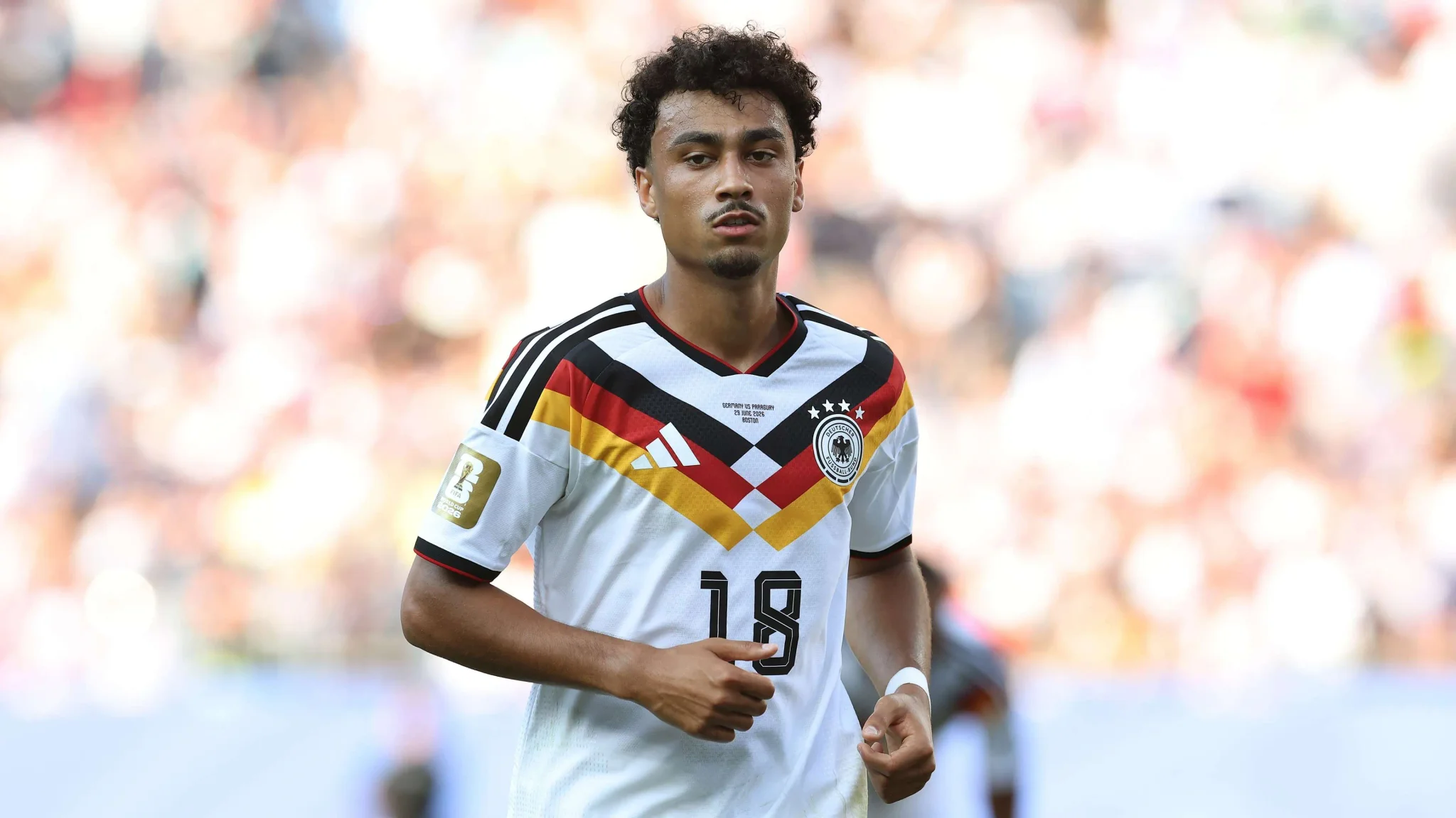 ناثانيال براون، المدافع الألماني الأمريكي، يرتدي قميص منتخب ألمانيا خلال مباراة دولية، مع تركيز على انتقاله إلى بايرن ميونخ وطموحه الرياضي.