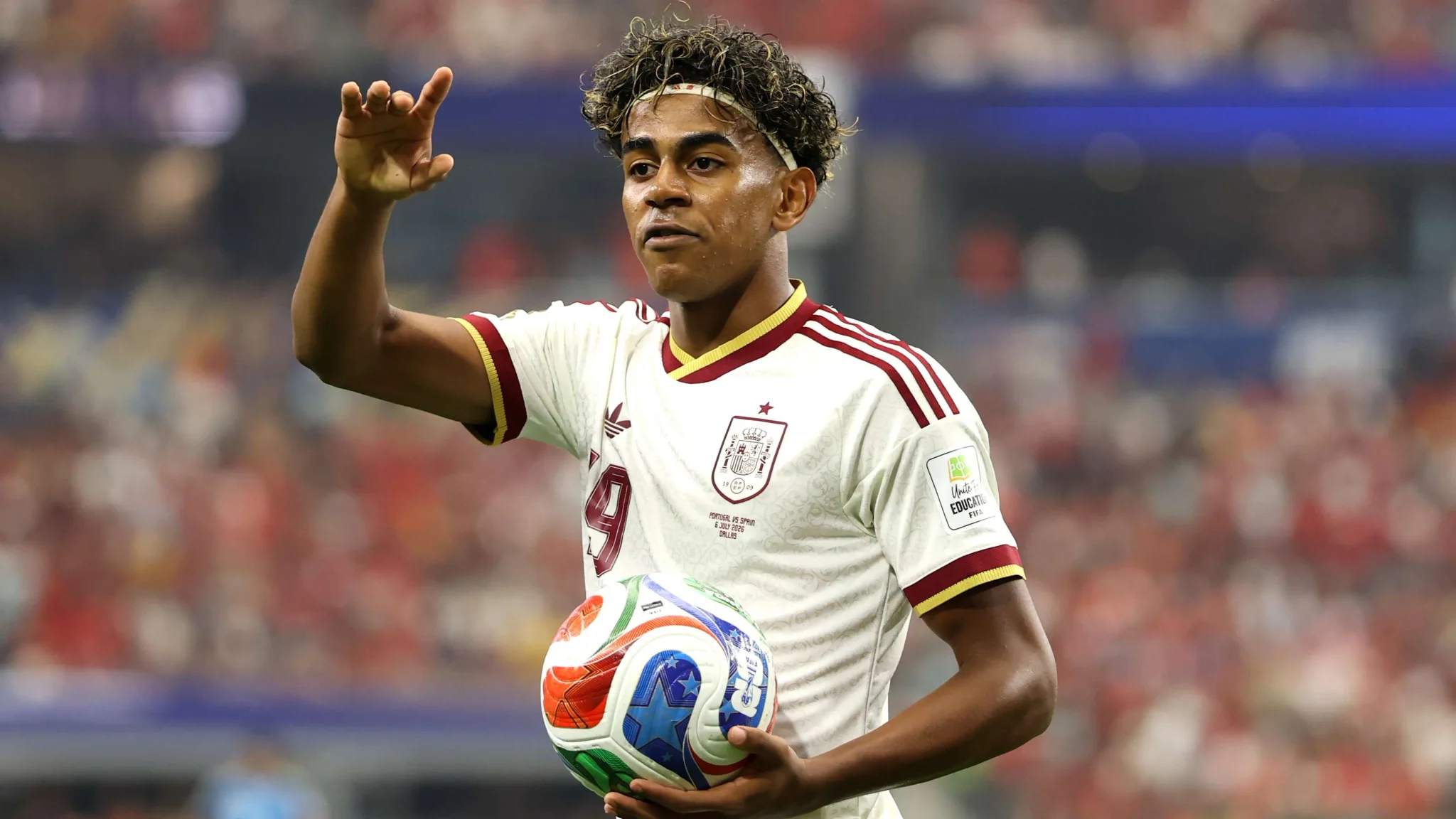 لاعب كرة قدم إسباني شاب يحمل الكرة استعداداً لتمريرها في مباراة كأس العالم ضد بلجيكا، مع تركيز على تحدي إيقاف فريق إسبانيا المتكامل.