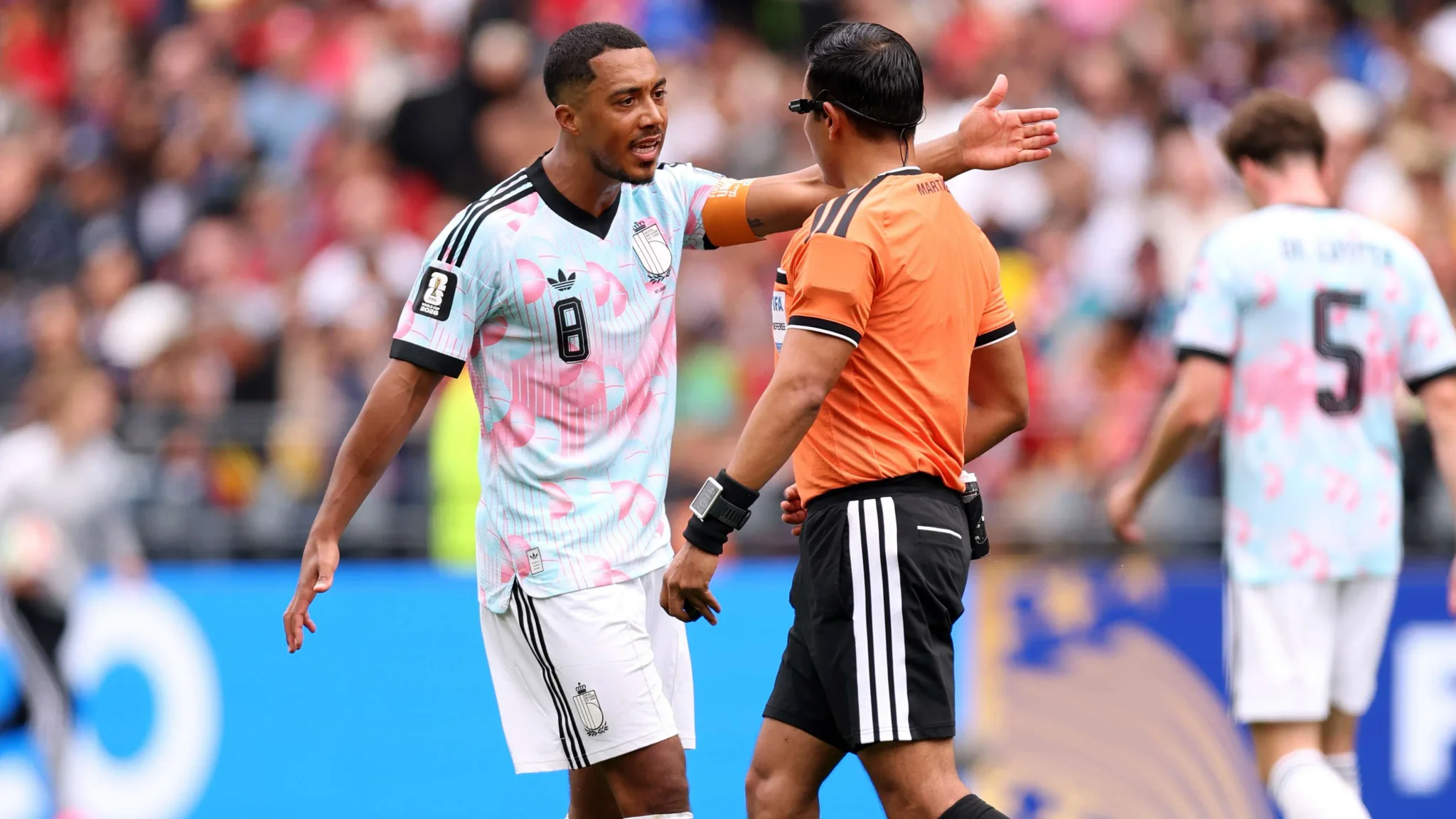لاعب كرة قدم من منتخب الأرجنتين يناقش الحكم أثناء مباراة في كأس العالم 2022، مع حضور لاعبين آخرين في الخلفية.