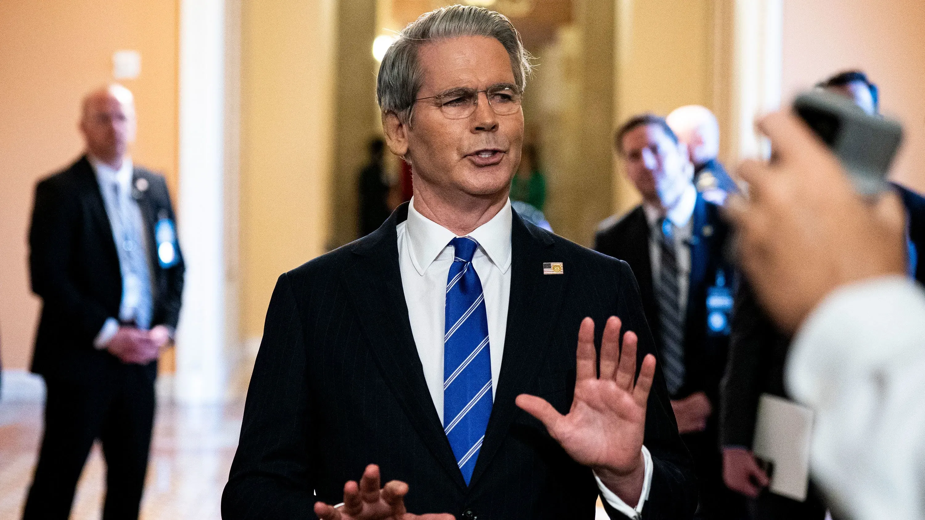 وزير الخزانة سكوت بيسنت يتحدث في مؤتمر، مع وجود حراس خلفه. يناقش مستقبل الاحتياطي الفيدرالي وتأثير الذكاء الاصطناعي على الاقتصاد.