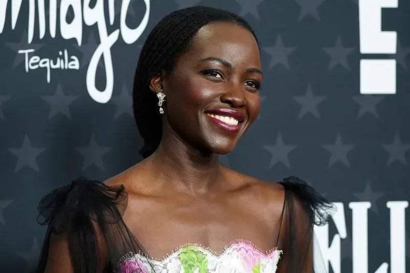 لويزا نيونغو مبتسمة في حفل توزيع الجوائز، ترتدي فستاناً مزيناً بألوان زاهية، مع خلفية تحمل شعار الحدث.