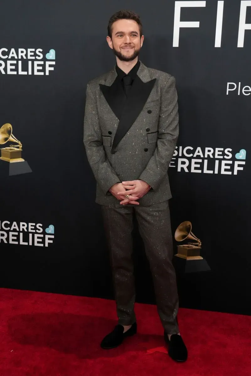 مغني يرتدي بدلة أنيقة ذات تصميم لامع، يقف مبتسمًا على السجادة الحمراء خلال حفل توزيع جوائز غرامي في لوس أنجلوس.