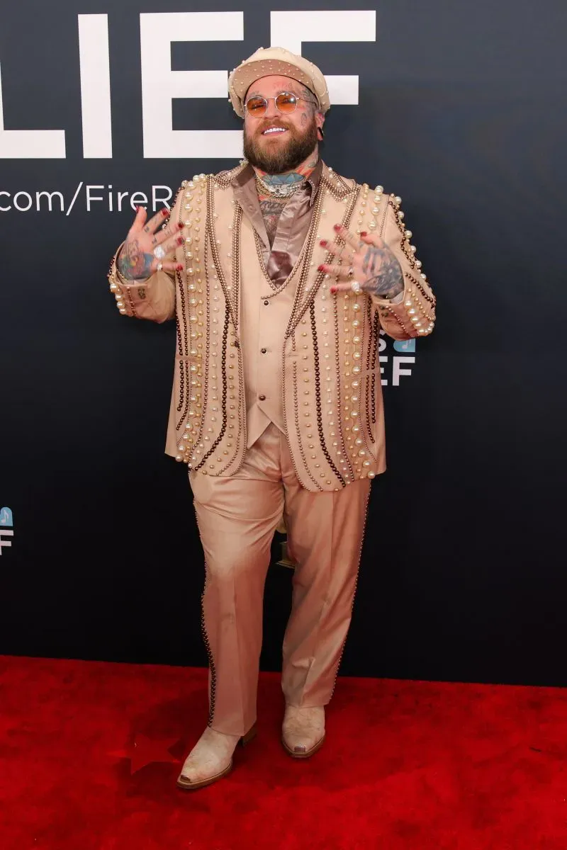 مظهر فني لشخص يرتدي بدلة مزينة بالخرز واللؤلؤ، يقف على السجادة الحمراء في حفل توزيع جوائز غرامي.