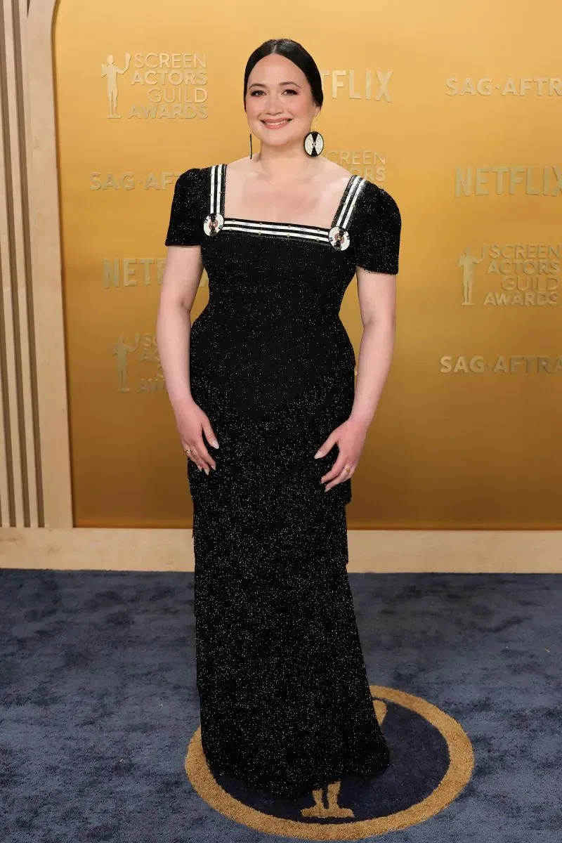 نجمة ترتدي فستانًا أسود أنيقًا مع تفاصيل بيضاء، مبتسمة على السجادة الحمراء في حفل توزيع جوائز نقابة ممثلي الشاشة.