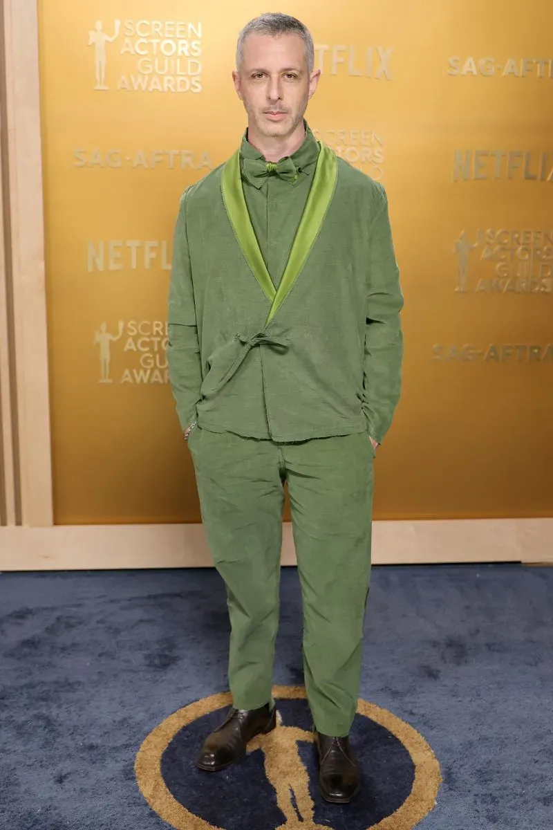 رجل يرتدي بدلة خضراء أنيقة يقف على السجادة الحمراء خلال حفل توزيع جوائز نقابة ممثلي الشاشة، مع خلفية تحمل شعار نتفليكس.