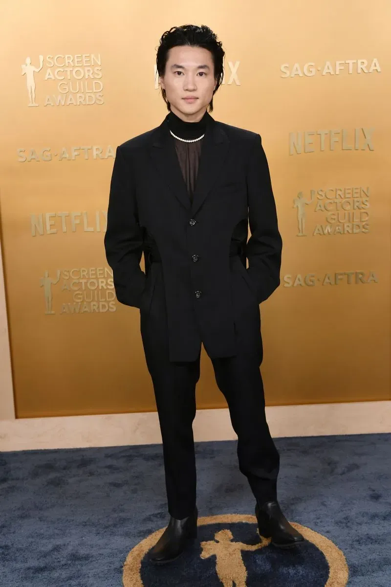 شخص يرتدي بدلة سوداء أنيقة مع تفاصيل عصرية، يقف على السجادة الحمراء خلال حفل توزيع جوائز نقابة ممثلي الشاشة.