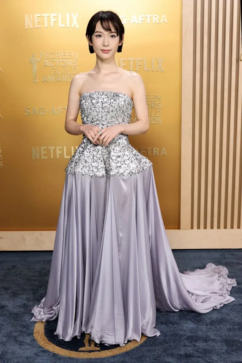 نجمة ترتدي فستانًا أنيقًا باللون الرمادي الفاتح مع تفاصيل لامعة، تتوسط السجادة الحمراء لحفل جوائز نقابة ممثلي الشاشة.