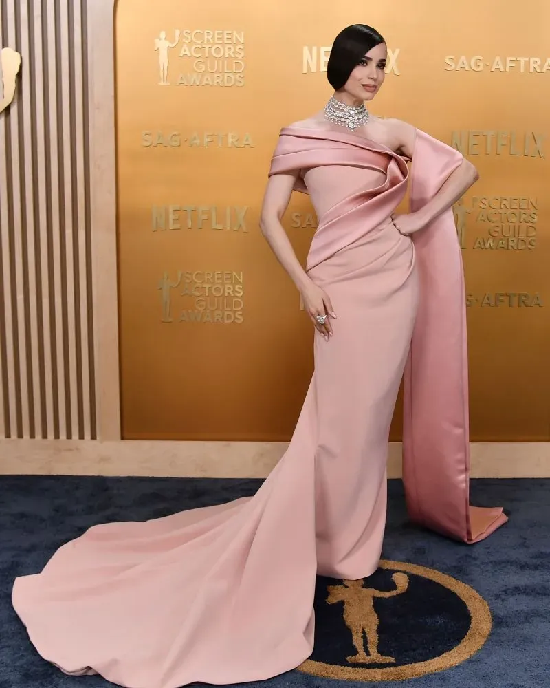 تظهر امرأة ترتدي فستاناً وردياً أنيقاً مع تفاصيل مميزة، في حفل توزيع جوائز نقابة ممثلي الشاشة، مع خلفية ذهبية تحمل شعارات الحدث.