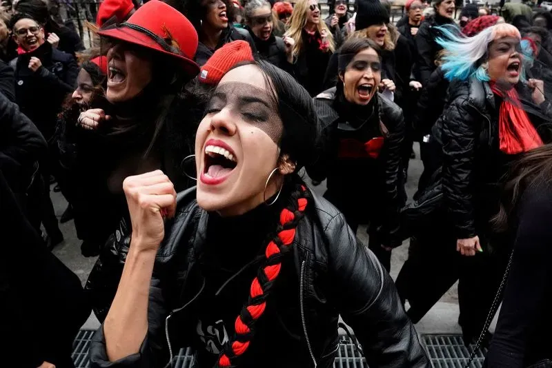 نساء يرتدين ملابس سوداء ويحتفلن بحركة #أنا_أيضًا، مع تعبيرات قوية من الحماس والدعم، أثناء مظاهرة للتنديد بالعنف الجنسي.