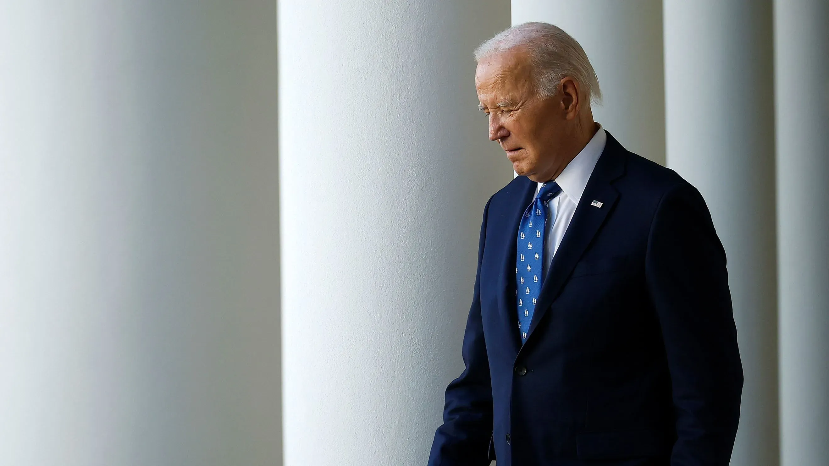 جو بايدن يسير في الممرات البيضاء للبيت الأبيض، يبدو عليه التأمل والجدية، مع التركيز على إنجازات إدارته في البنية التحتية والإغاثة من كوفيد.