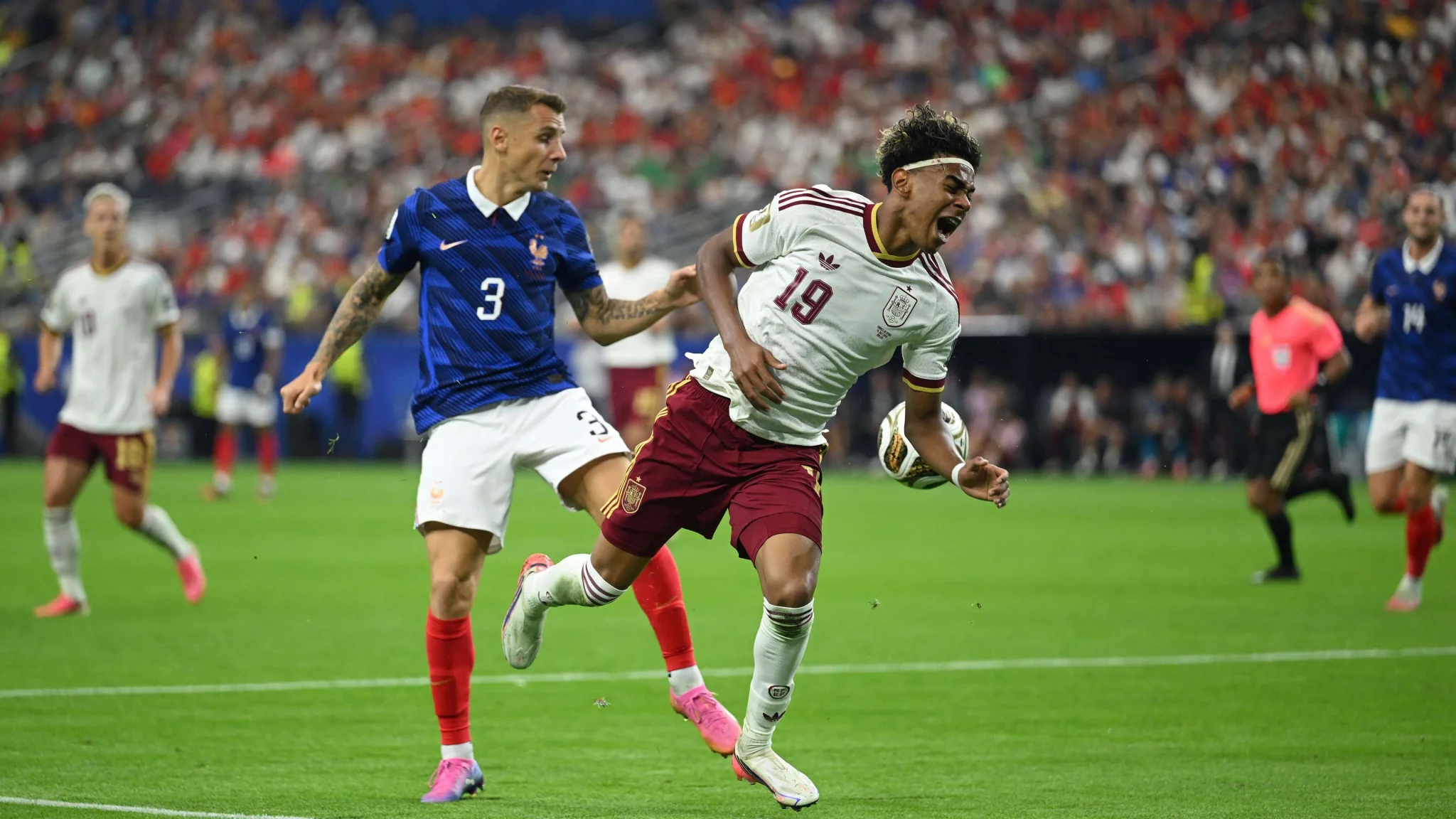 لاعب كرة قدم إسباني يرتدي قميص رقم 19 يتعرض لإعاقة من لاعب فرنسي في مباراة كأس العالم 2026 وسط حماس الجماهير.