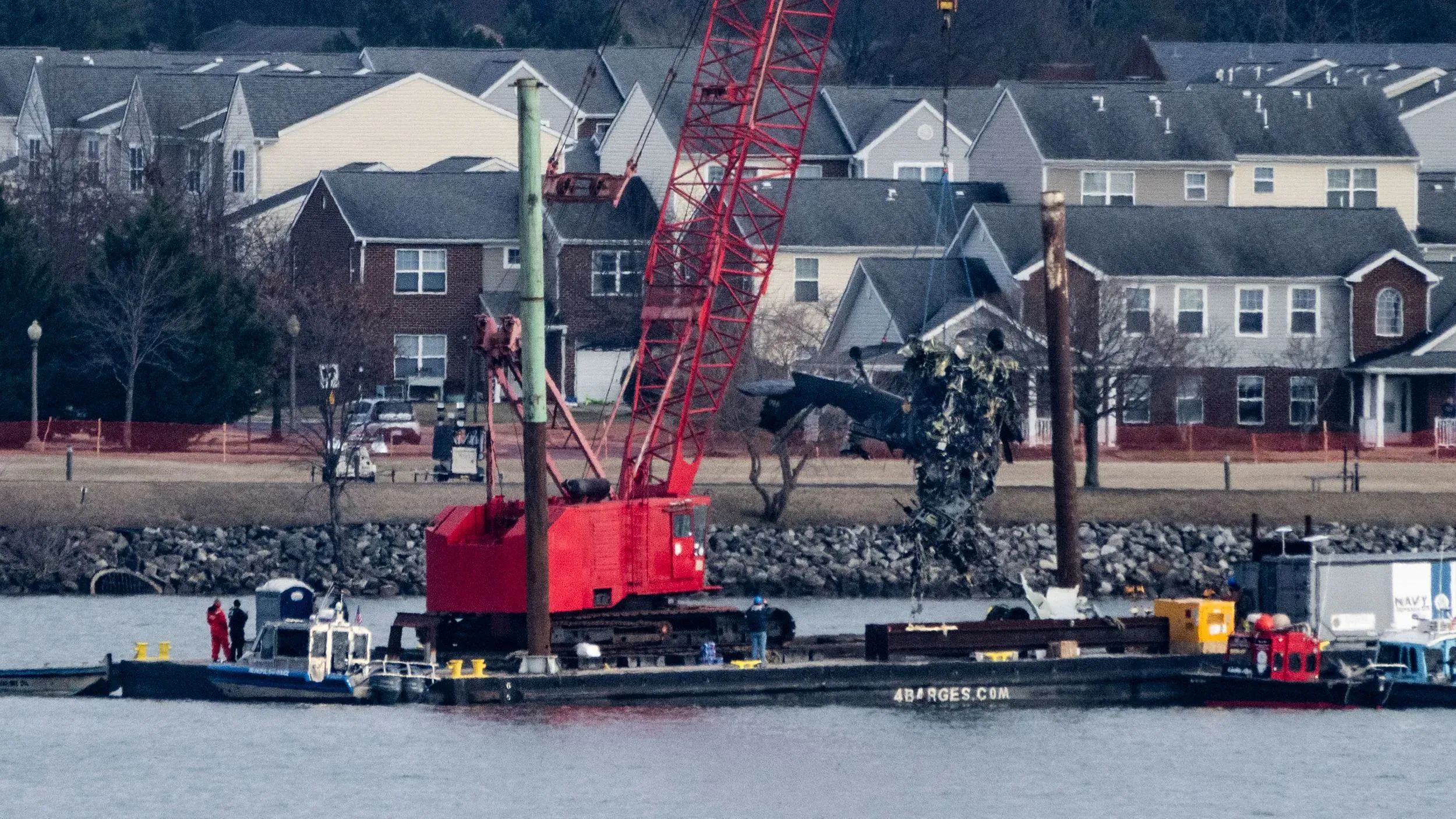 رفع حطام مروحية بلاك هوك من النهر بواسطة رافعة حمراء، مع وجود فرق الإنقاذ على متن قارب بالقرب من الشاطئ.