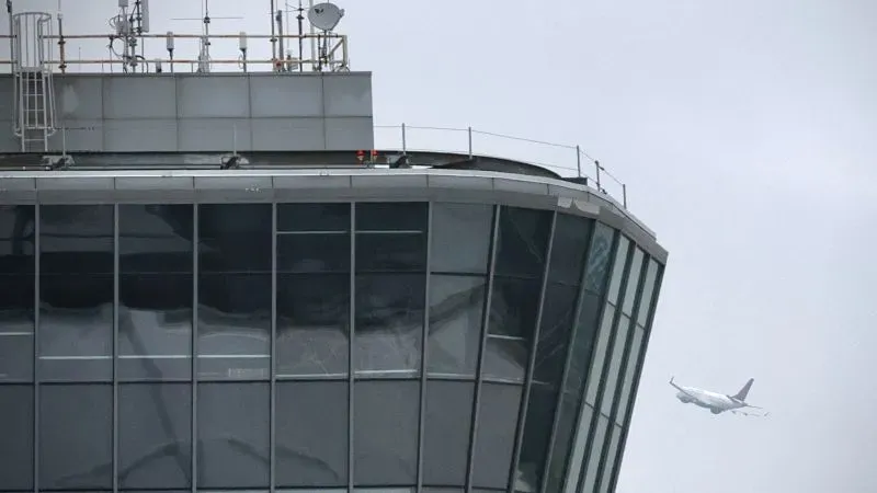 برج مراقبة حركة الطيران في مطار مع طائرة تمر بالقرب منه، يعكس التحديات التقنية التي تواجه سلامة الطيران في الولايات المتحدة.