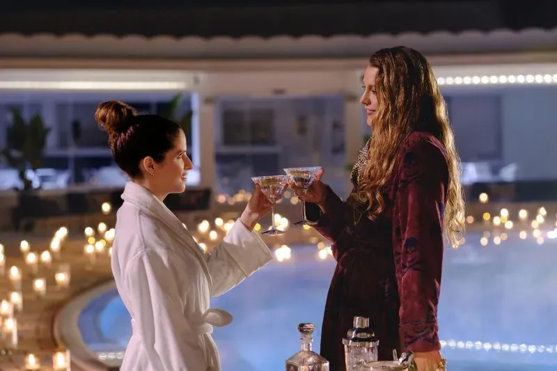 مشهد من فيلم "خدمة بسيطة أخرى" يظهر إيميلي وستيفاني يتبادلان التحية بكأسين من الكوكتيل بجوار حمام السباحة، مع أجواء رومانسية مضاءة بالشموع.