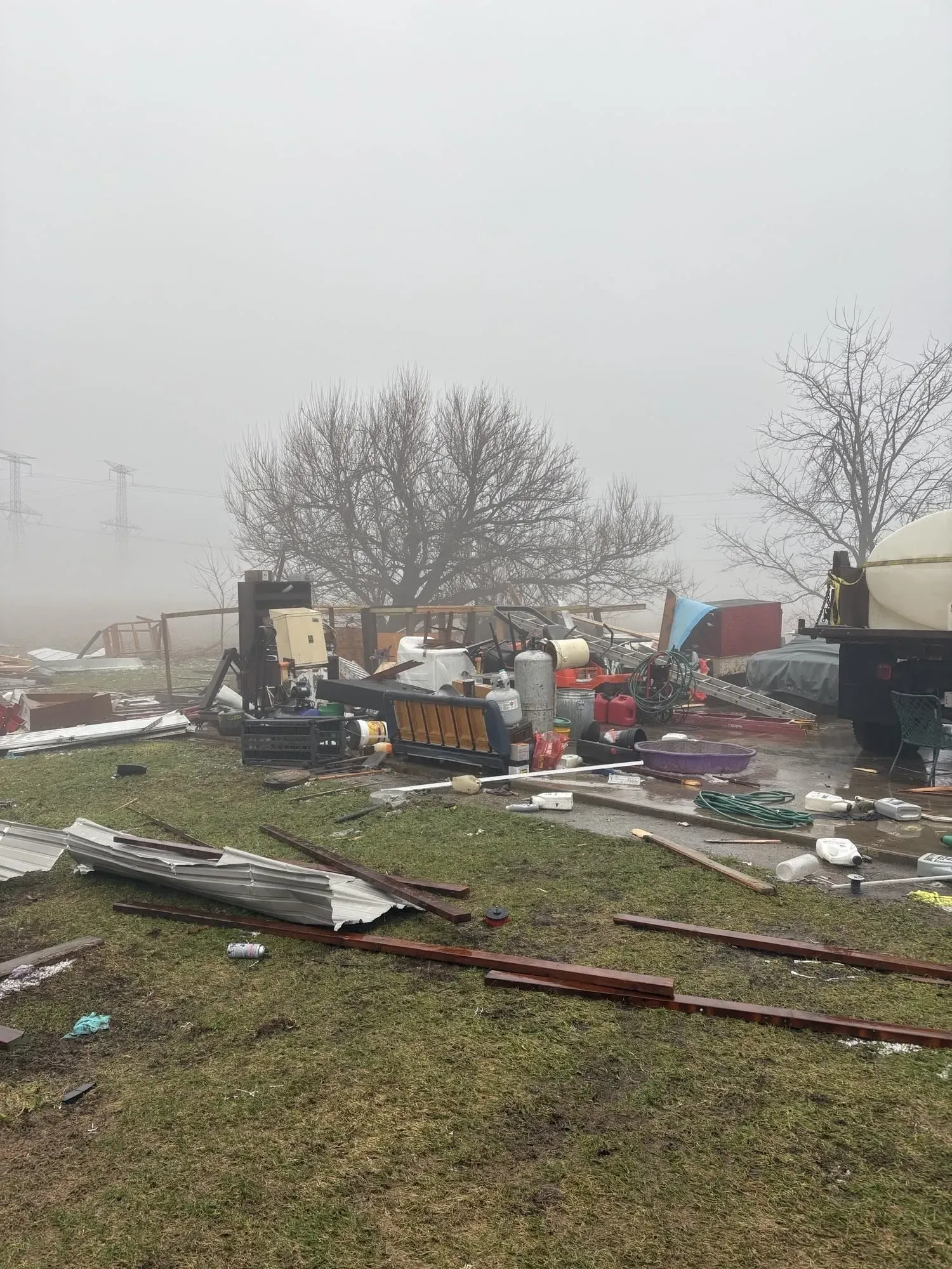 تظهر الصورة مشهدًا فوضويًا لآثار عاصفة شتوية، مع حطام متناثر وأشجار عارية في بيئة ضبابية، مما يعكس الأضرار الناتجة عن الطقس القاسي.