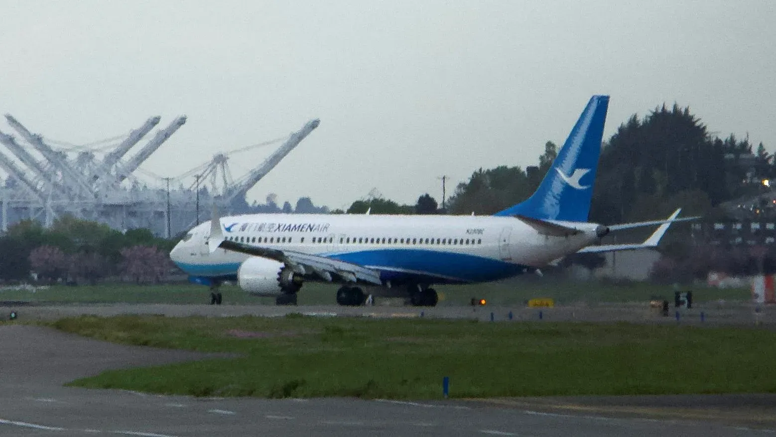 هبوط طائرة بوينج 737 ماكس المخصصة لشركة شيامن الجوية في مطار بوينج في سياتل، وسط خلفية لمرافق الطيران.