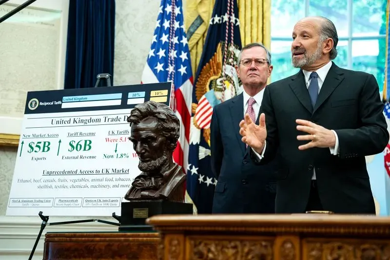 تظهر الصورة مسؤولين يتحدثون أمام لوحة توضح تفاصيل صفقة تجارية مع المملكة المتحدة، مع تمثال لأبراهام لينكولن في المقدمة.