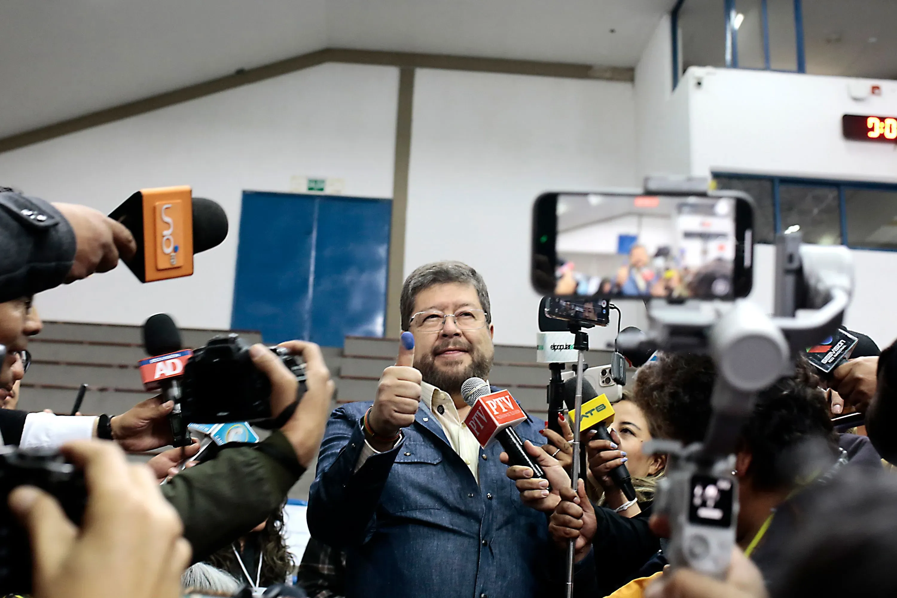 السيناتور رودريغو باز يبتسم ويشير بإبهامه في تجمع صحفي بعد نتائج الانتخابات الرئاسية، محاطًا بالصحفيين والكاميرات.