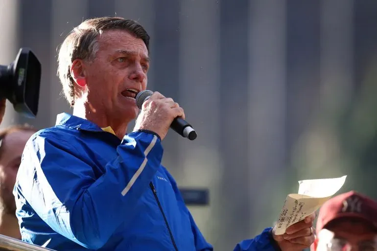 الرئيس البرازيلي السابق جايير بولسونارو يتحدث في تجمع عام، محاطًا بجمهور، مع ورقة في يده، مع التركيز على قضايا سياسية مثيرة للجدل.