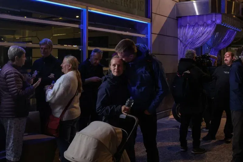 مجموعة من الأشخاص يتجمعون في الخارج، بعضهم يتحدث بينما يحمل آخرون زجاجات مياه، في أجواء هادئة بعد حادث انفجار في أثينا.