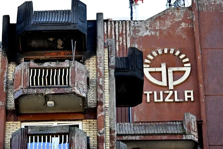 واجهة دار للمسنين في توزلا، البوسنة، تظهر الأضرار الناجمة عن حريق مميت، مع شعار "توزلا" واضح على الجدار.