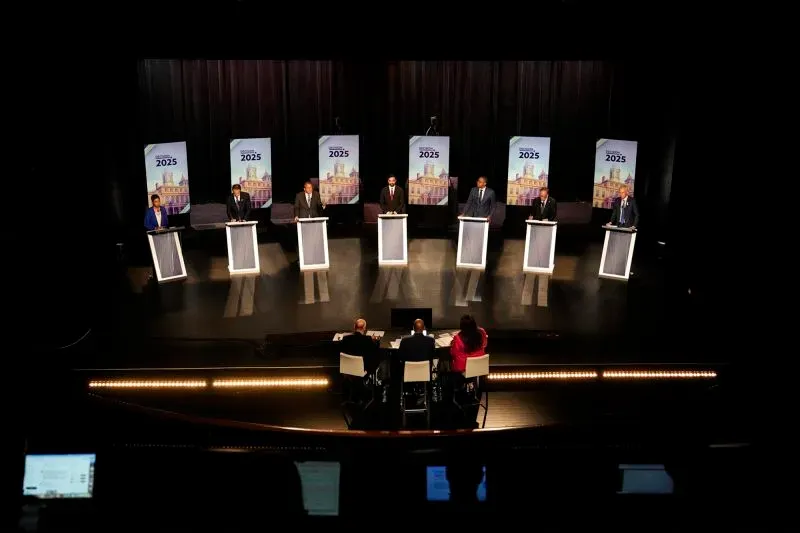 مناظرة انتخابية في نيويورك عام 2025، حيث يتواجد عدة مرشحين خلف منصات، مع وجود لجنة تحكيم في الأسفل.