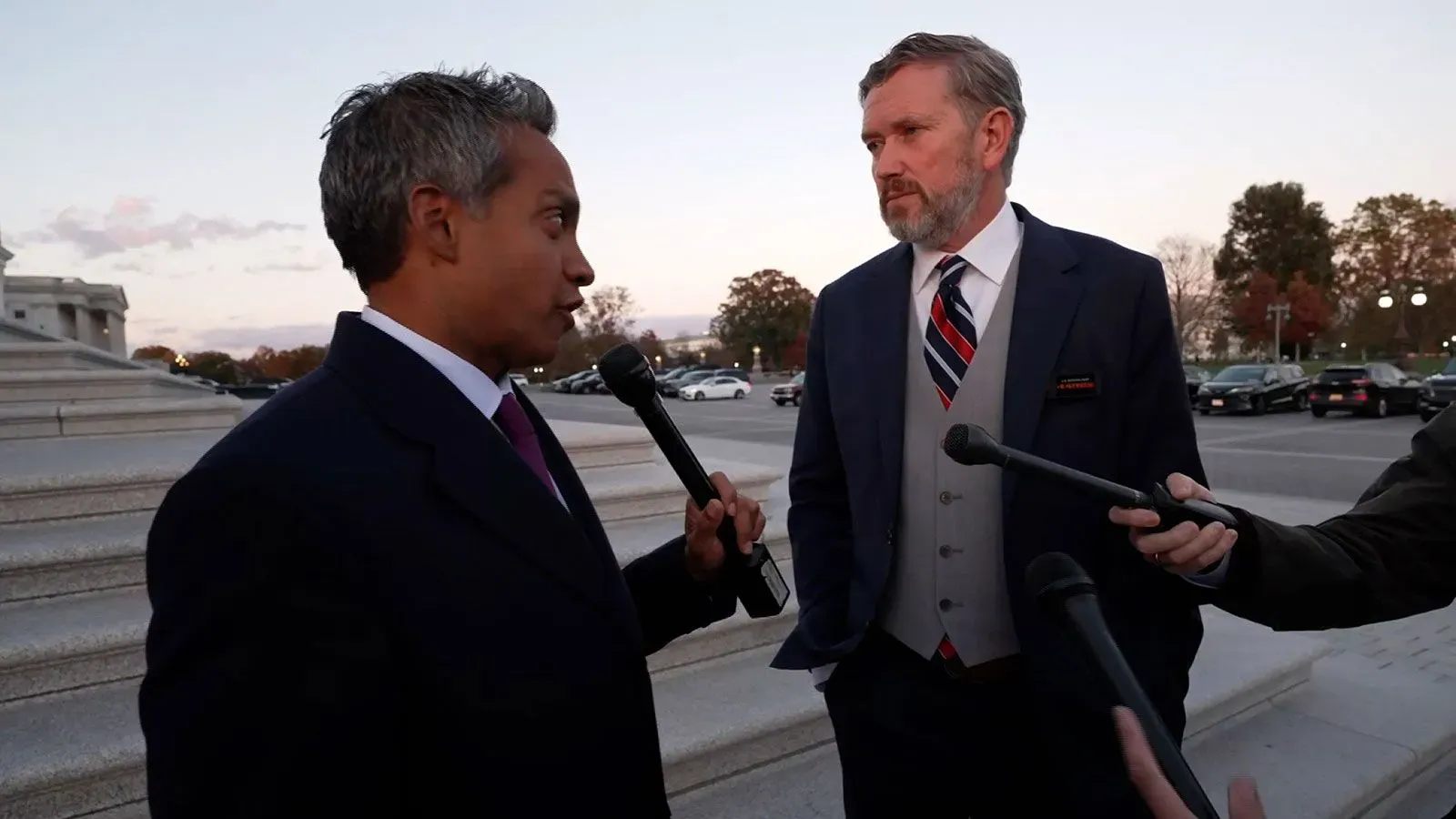 مقابلة صحفية خارج مبنى الكونغرس، حيث يتحدث رجلان يرتديان بدلات، مع وجود صحفيين ومعدات تصوير حولهما.
