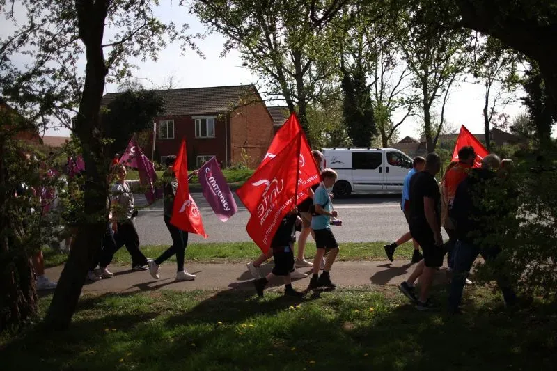 محتجون يحملون لافتات حمراء، يسيرون في شارع بالقرب من منازل، تعبيرًا عن دعمهم لصناعة الصلب في سكونثورب بعد تدخل الحكومة.