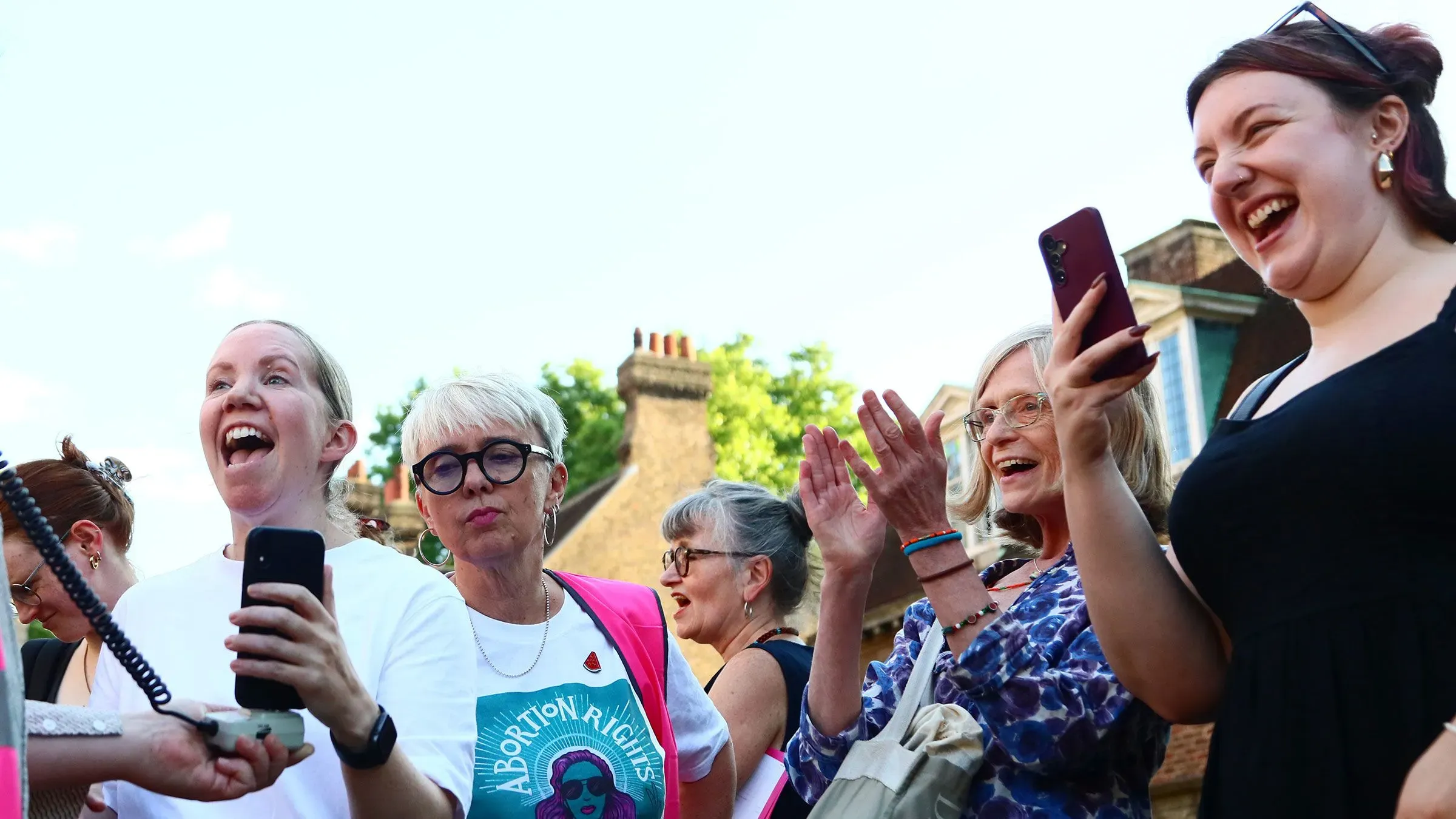 نساء يبتسمن ويحتفلن في تجمع لدعم حقوق الإجهاض، مع لافتة تحمل عبارة "حقوق الإجهاض"، تعبيرًا عن تأييدهن للتغييرات القانونية في المملكة المتحدة.