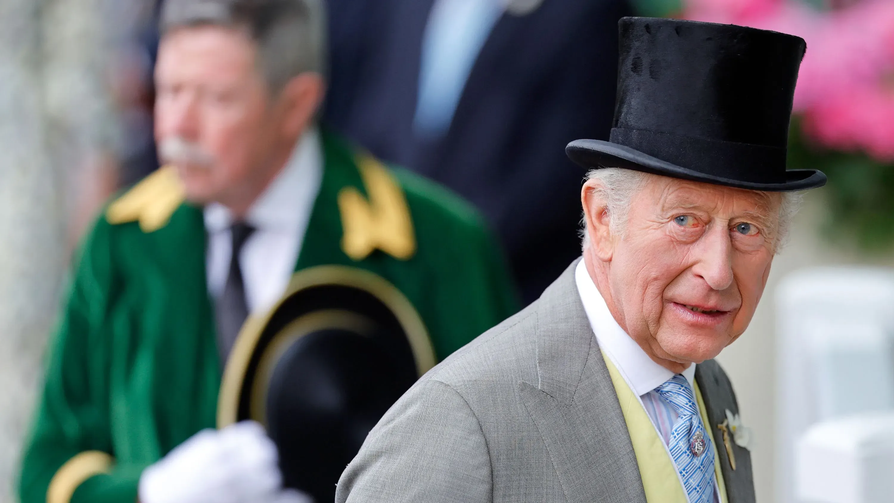 الملك تشارلز الثالث يرتدي بدلة رسمية وقبعة عالية، مع وجود شخص آخر خلفه، في مناسبة رسمية تعكس التقاليد الملكية.