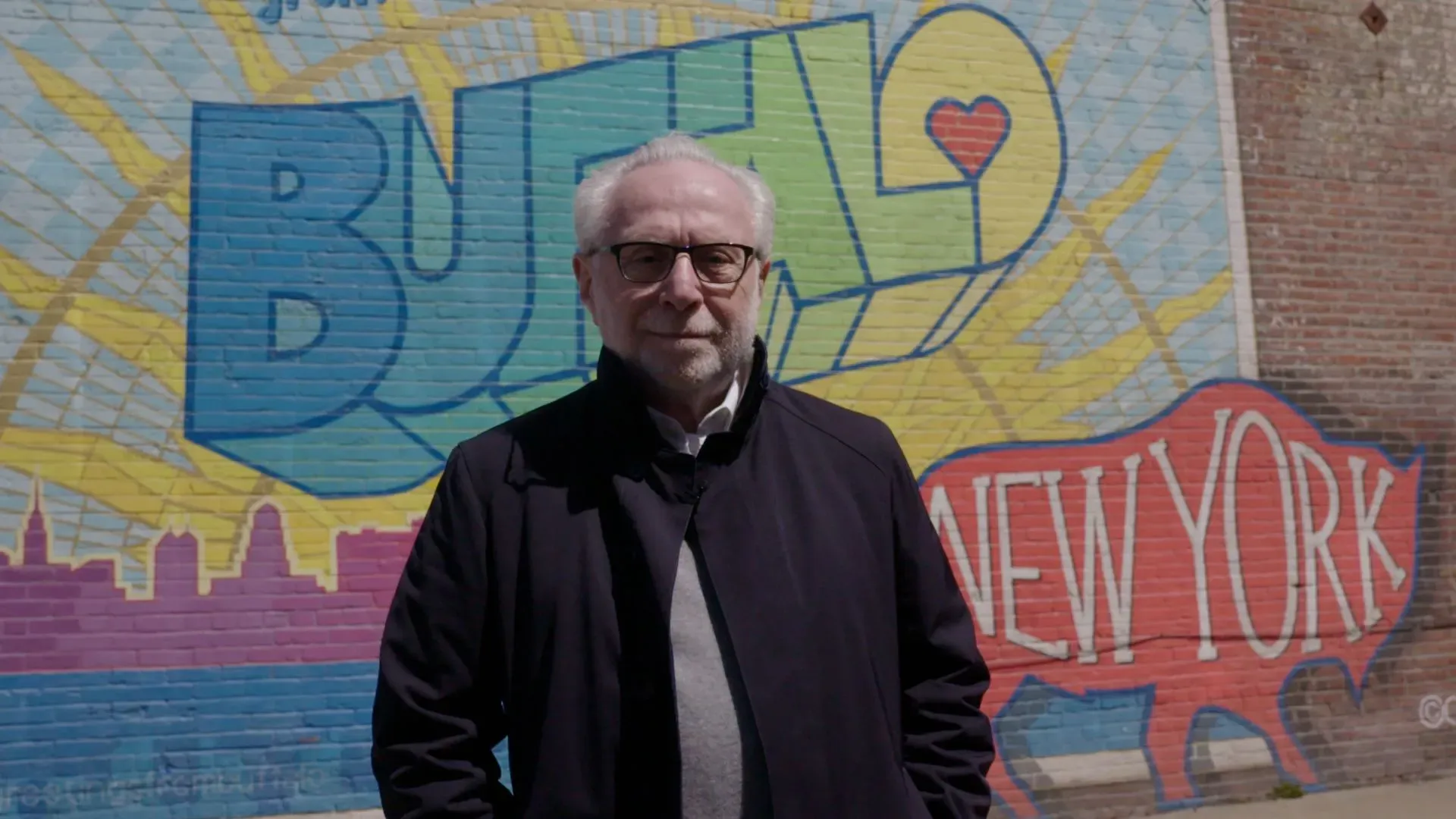 رجل مسن يقف أمام جدار ملون يحمل عبارة "بافالو نيويورك"، يعكس روح المدينة وحماس سكانها لفريقهم المحلي.