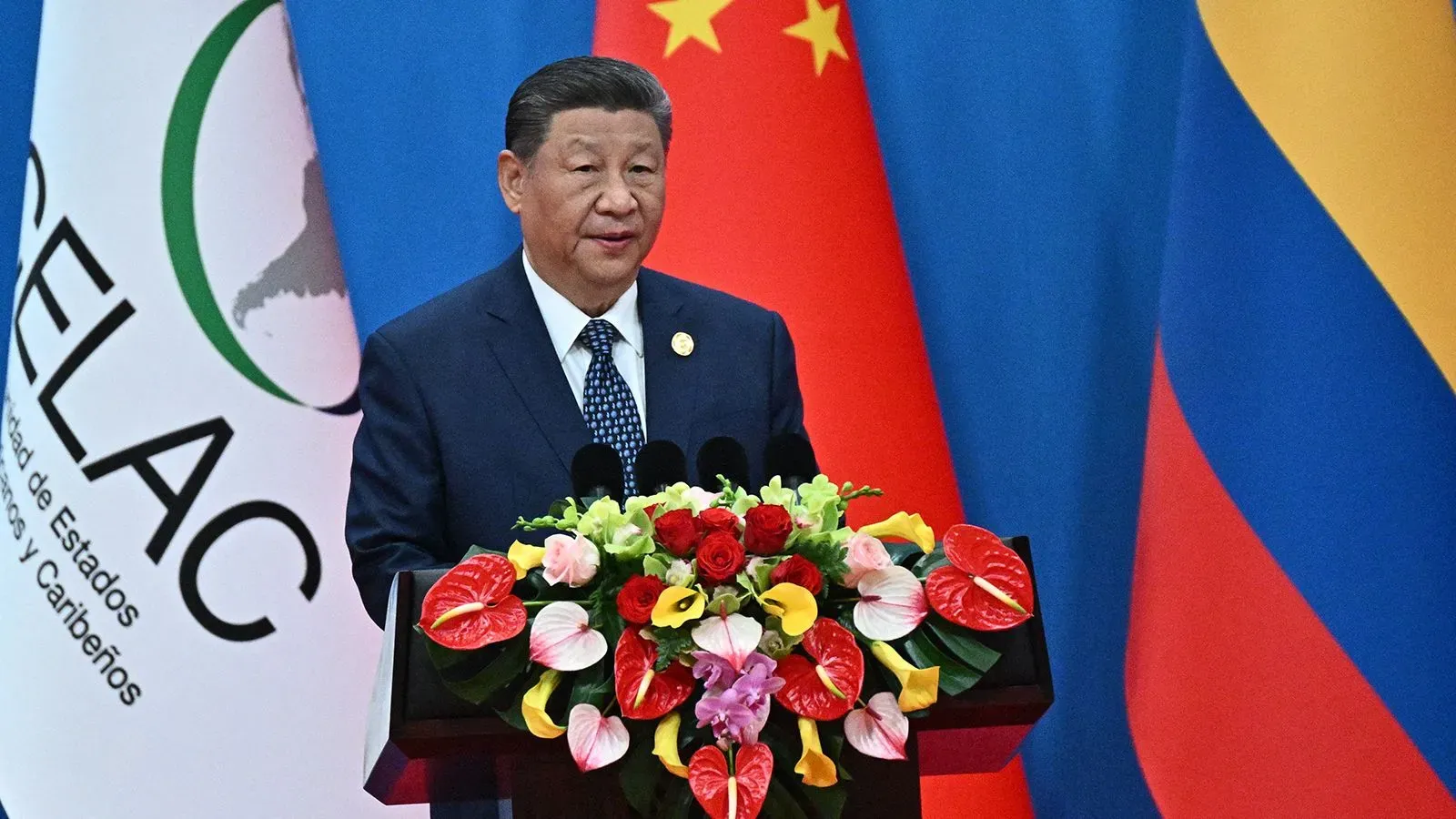 شي جين بينغ يلقي خطابًا في قمة بأمريكا اللاتينية، مع باقة زهور ملونة خلفه، مشددًا على أهمية التعاون الدولي في ظل التوترات التجارية.