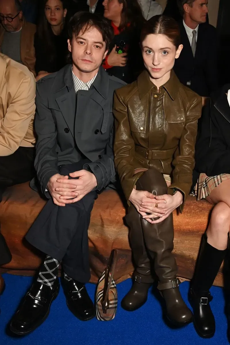 صورة لممثلين يجلسان في الصف الأمامي خلال عرض أزياء بربري لموسم خريف وشتاء 2025، يرتديان ملابس عصرية بألوان محايدة.