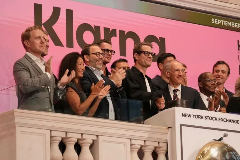احتفال فريق شركة Klarna بإدراجها في بورصة نيويورك، مع وجود شعار الشركة خلفهم، في حدث يبرز نجاح الطرح العام الأولي.
