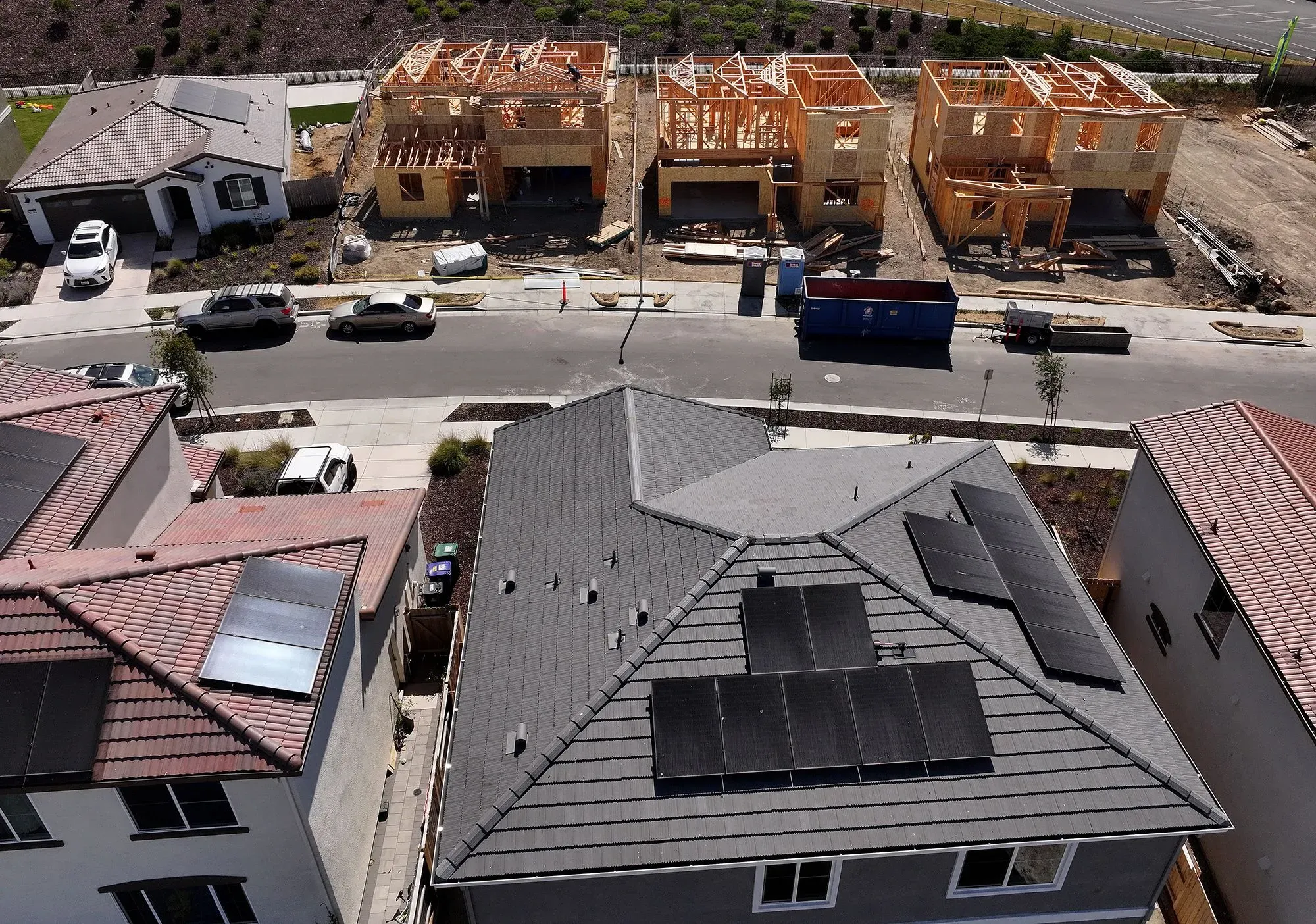 صورة جوية توضح منازل جديدة قيد الإنشاء في حي سكني، مع منازل قائمة تحتوي على ألواح شمسية، تعكس التغيرات في سوق الإسكان.