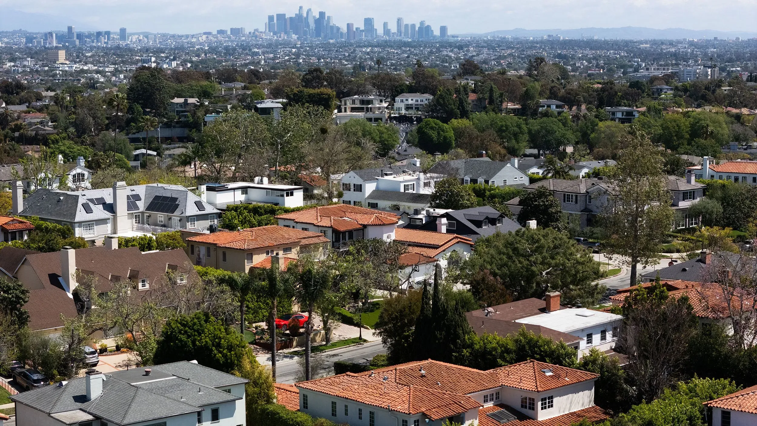 منظر جوي لحي سكني في الولايات المتحدة، يظهر منازل مختلفة مع خلفية لمدينة، يعكس ارتفاع تكاليف ملكية المنازل بعد جائحة كوفيد-19.