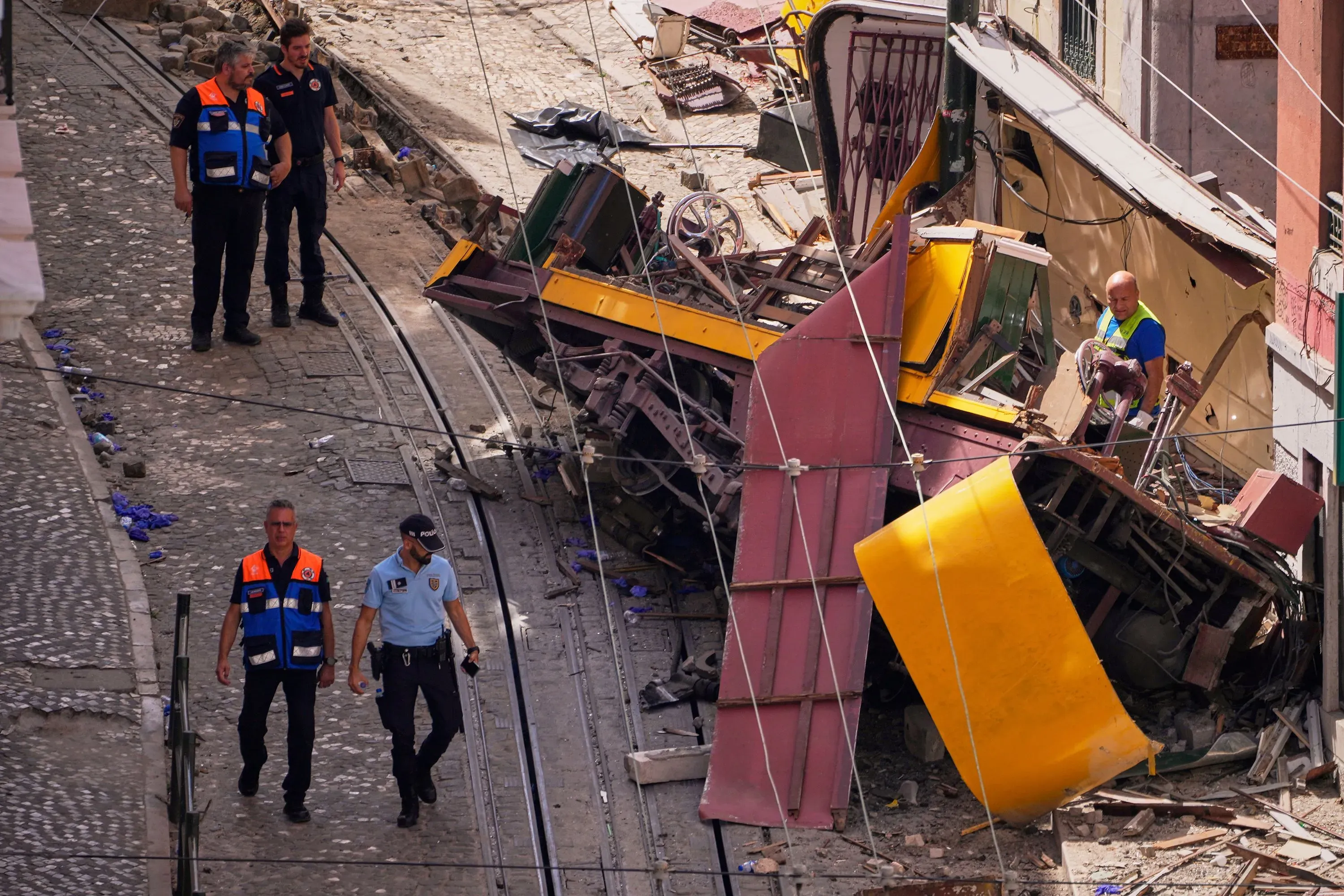 حادث قطار جبلي مائل في لشبونة، يظهر رجال الإنقاذ يتفقدون العربة المقلوبة على الأرض، مع آثار الدمار في الخلفية.
