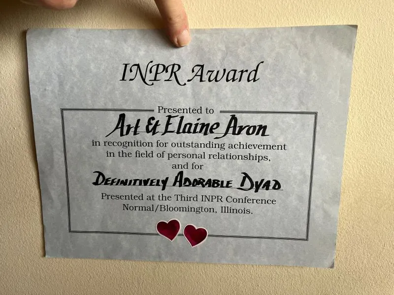 شهادة تقدير تُظهر جائزة INPR مُقدمة لآرثر وإيلين آرون تقديراً لإنجازاتهما في مجال العلاقات الشخصية، مع قلوب حمراء في الأسفل.