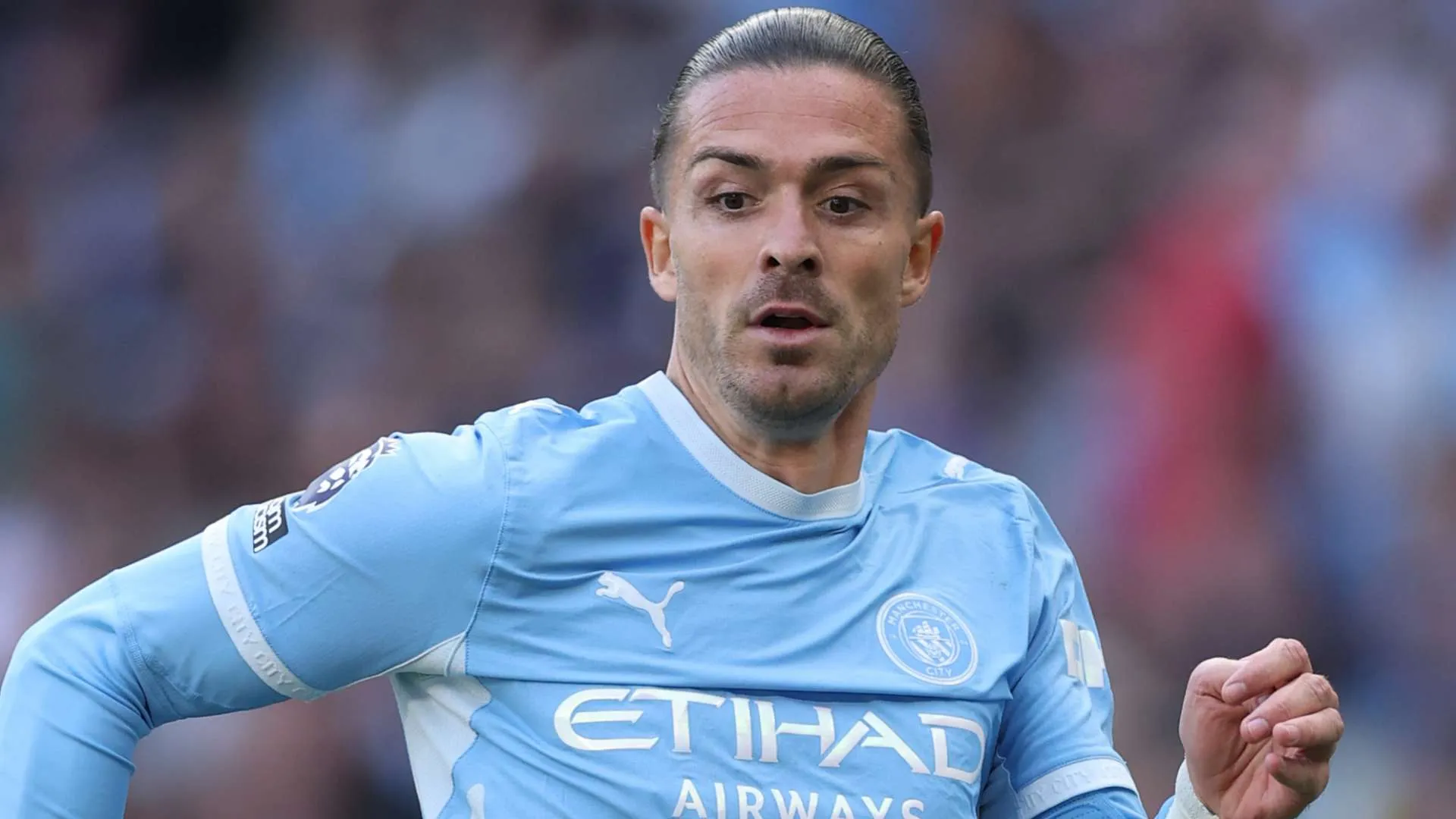 جاك جريليش لاعب مانشستر سيتي يرتدي القميص الأزرق أثناء مباراة في الدوري الإنجليزي الممتاز، مع تركيز على وجهه وحركته في الملعب.