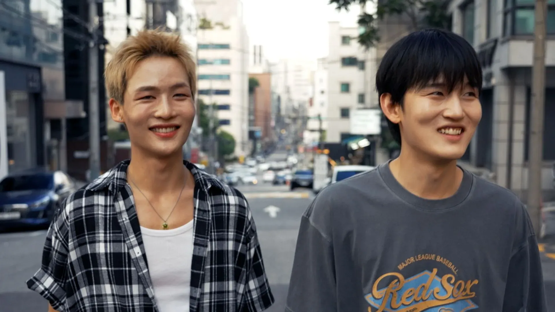 سيوك وهيوك، عضوا فرقة 1VERSE، يسيران في شوارع سيول مبتسمين، يعكسان طموحهم في عالم البوب الكوري بعد رحلتهم من كوريا الشمالية.