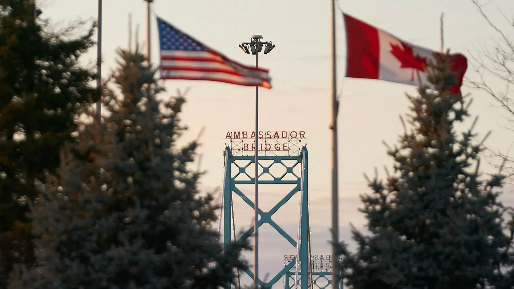 جسر السفير يربط بين كندا والولايات المتحدة، مع أعلام البلدين ترفرف في الخلفية، مما يعكس أهمية الحدود والتفتيش الأمني.