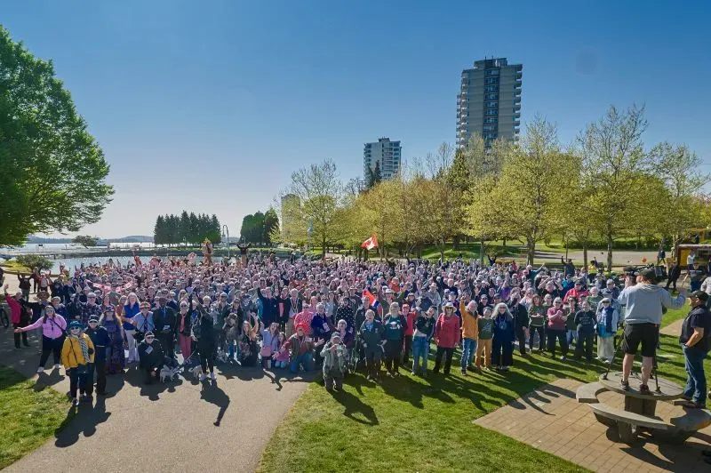 تجمع حشد كبير من الزوار في حديقة تحت أشعة الشمس، مع العلم الكندي في الخلفية، احتفالاً بالترحيب بالسياح الأمريكيين في كندا.