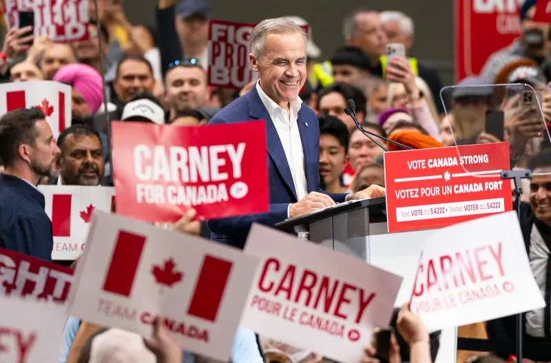 مارك كارني يتحدث في تجمع انتخابي حاشد وسط حشود من المؤيدين، مع لافتات تدعم حملته "كارني من أجل كندا" في خلفية الصورة.