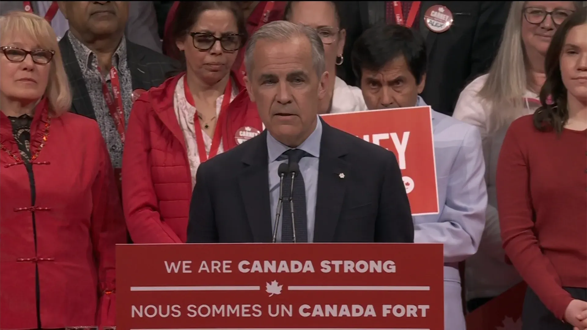 مارك كارني يتحدث أمام حشد من أنصاره بعد الانتخابات، مع لافتة "نحن كندا قوية" خلفه، مع تعبيرات جادة من الحضور.