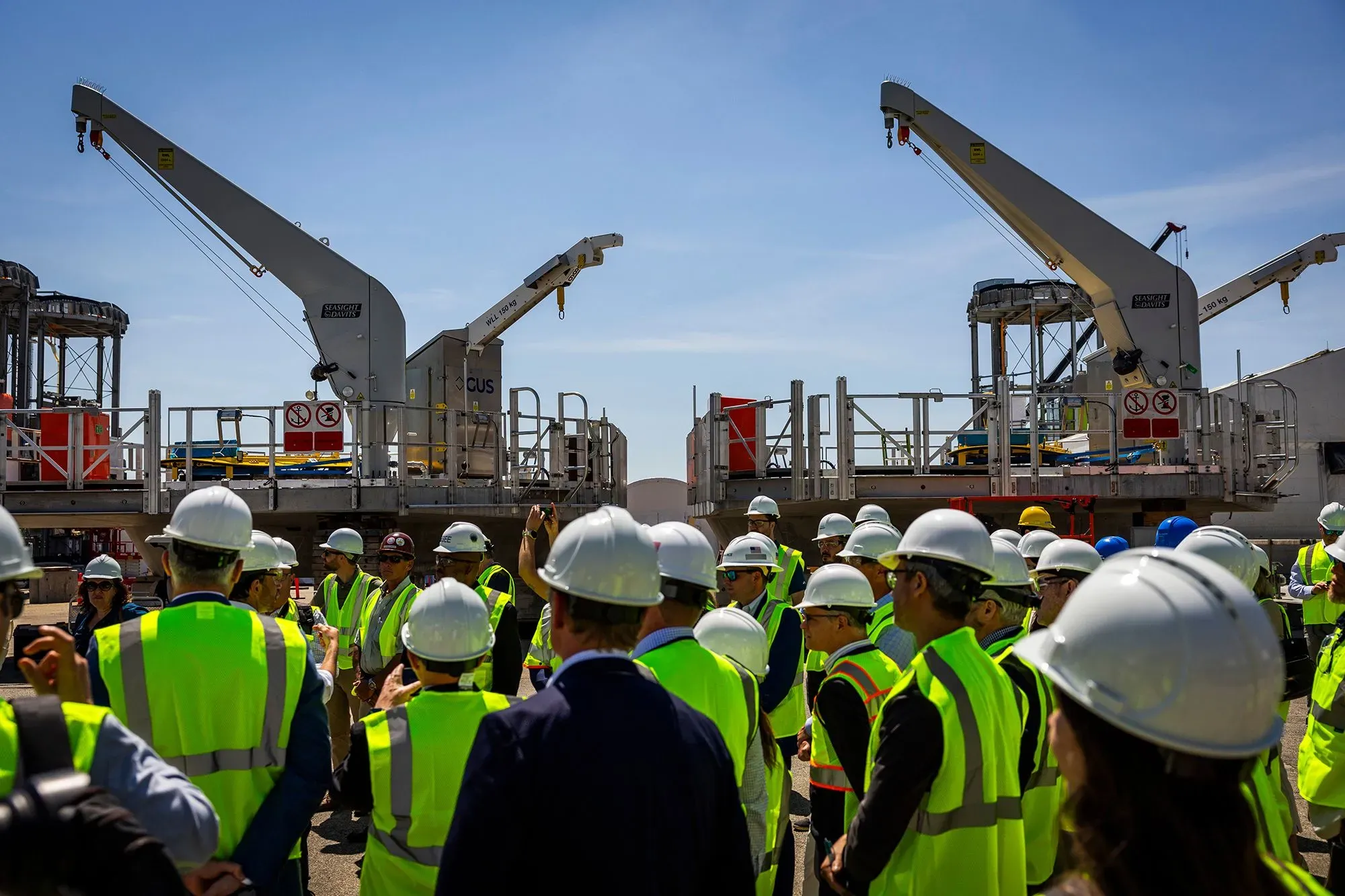 مجموعة من العمال مع معدات بناء في موقع مشروع طاقة الرياح "Revolution Wind" في رود آيلاند، مع التركيز على الآلات المستخدمة في المشروع.