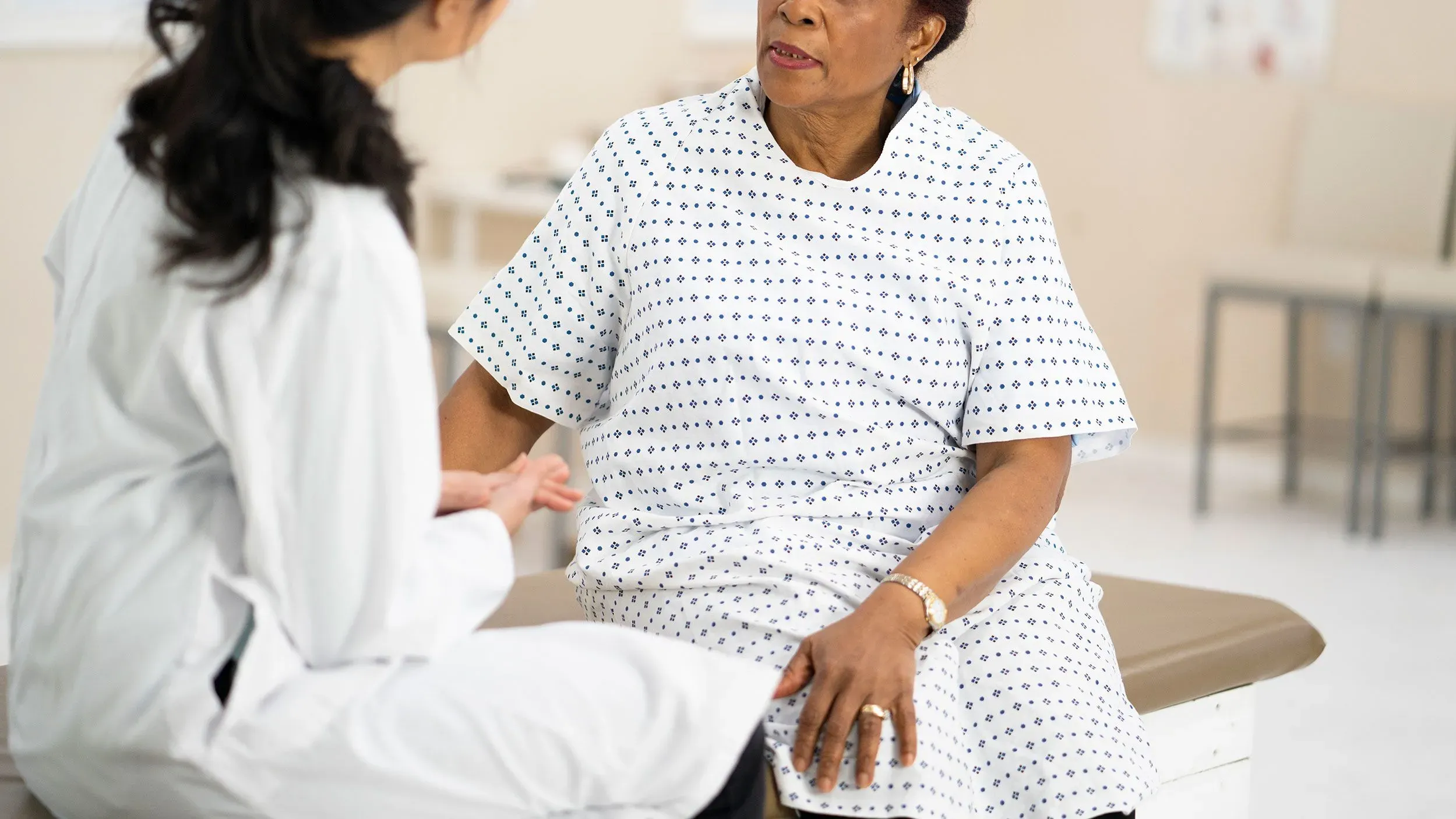 امرأة ترتدي ملابس طبية تجلس في عيادة طبية، تتحدث مع طبيبة، مما يعكس أهمية الفحص المبكر للكشف عن السرطان.